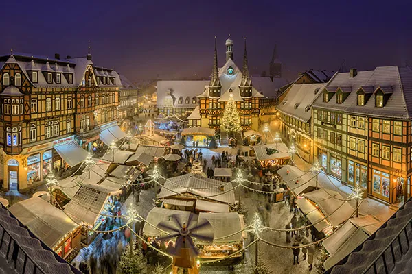 Wernigerode Weihnachtsmarkt in der Altstadt. Die nächtliche Szene zeigt einen belebten Weihnachtsmarkt mit gut beleuchteten Ständen auf einem zentralen Platz, der von traditionellen Fachwerkhäusern umgeben ist.