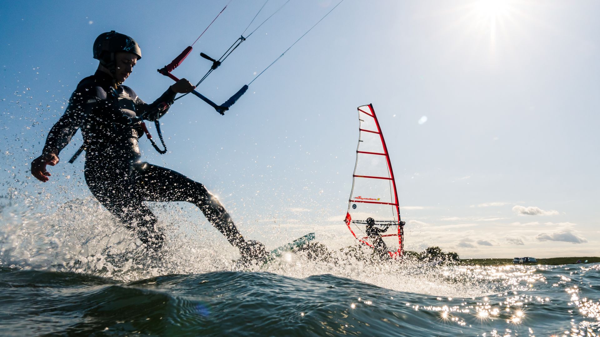 Kitesurfers and windsurfers on the water against the light of the sun