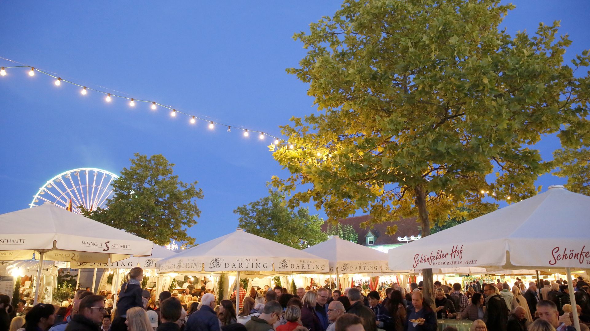 Soirée animée à la fête avec des stands illuminés, de nombreux visiteurs et une grande roue en arrière-plan
