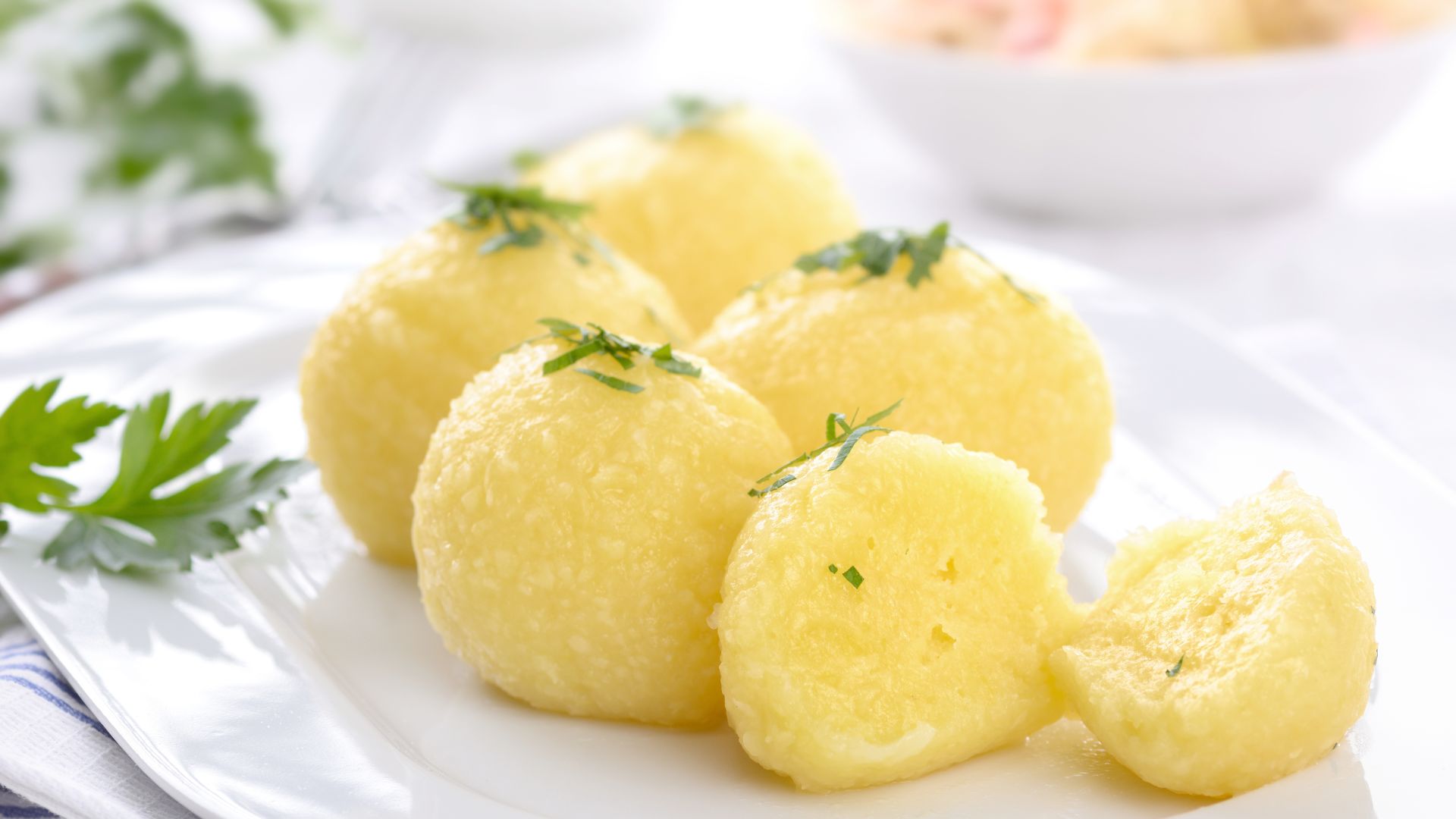 Kartoffelknödel sind auf einem weißen Teller mit einem Stück Petersilie als Garnitur angerichtet.