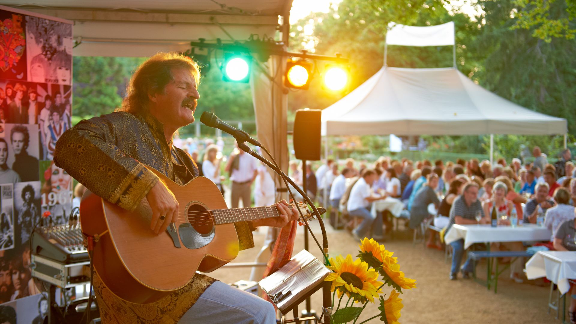 Un musicien joue de la guitare et chante au coucher du soleil sur le marché aux vins de Mayence, tandis que les invités sont assis à de longues tables sous des pavillons et profitent de l`ambiance.