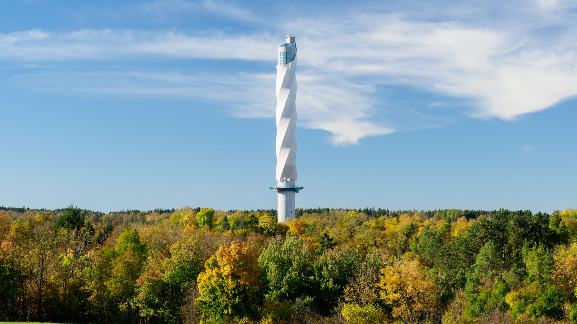 Der Rottweil-Turm, ein moderner Aussichtsturm mit einer markanten, spiralförmigen Architektur, erhebt sich vor dem Hintergrund von buntem Herbstwald und einem klaren blauen Himmel