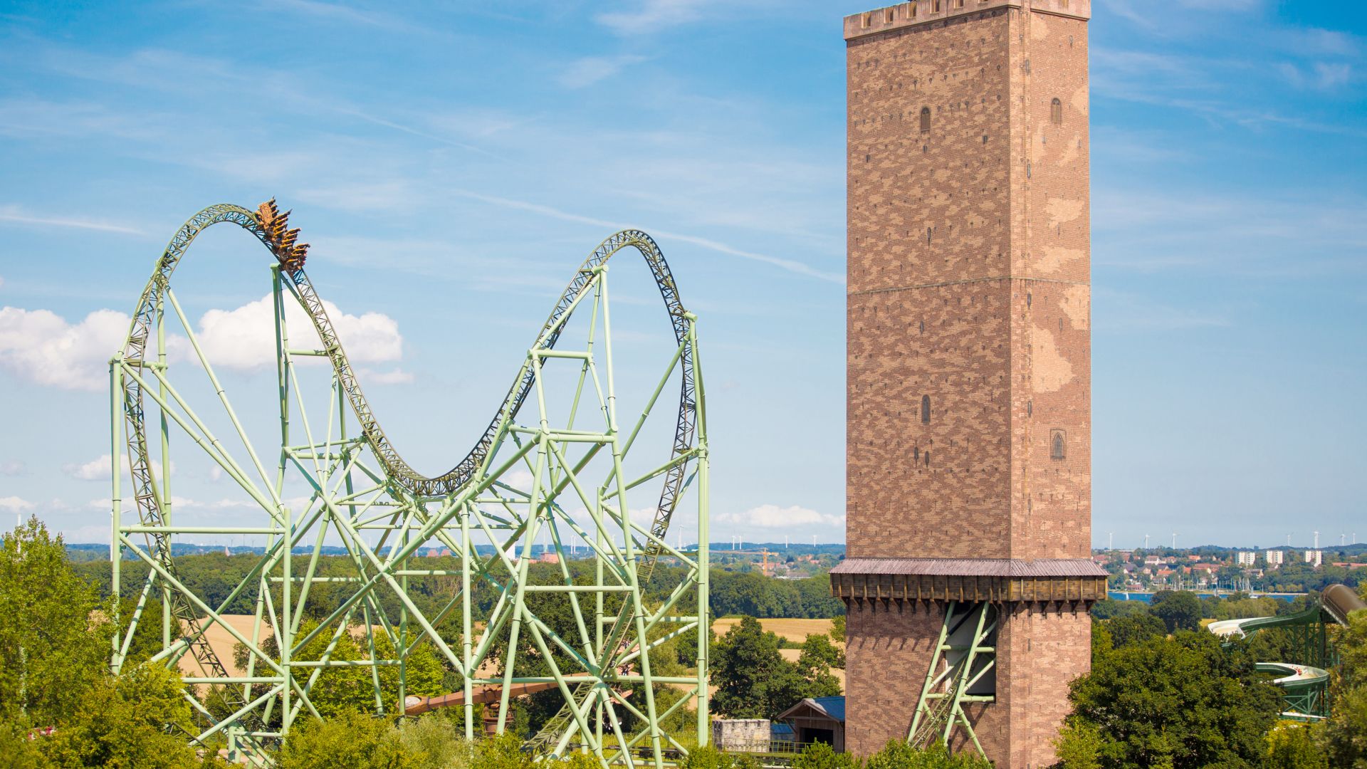 Blick auf eine Achterbahn neben einem großen Backsteinturm