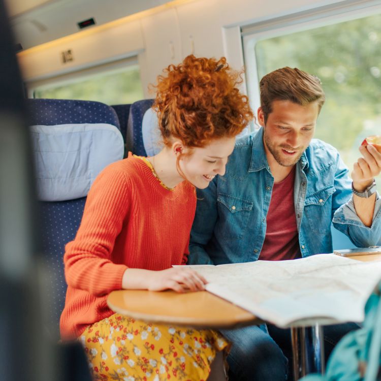 Man and woman reading a map of Germany while travelling on an ICE train ©DZT (Julia Nimke) Ein Mann und eine Frau sitzen zusammen in einem Zug. Sie schauen auf eine Deutschlandkarte, die vor ihnen auf einem Tisch liegt.