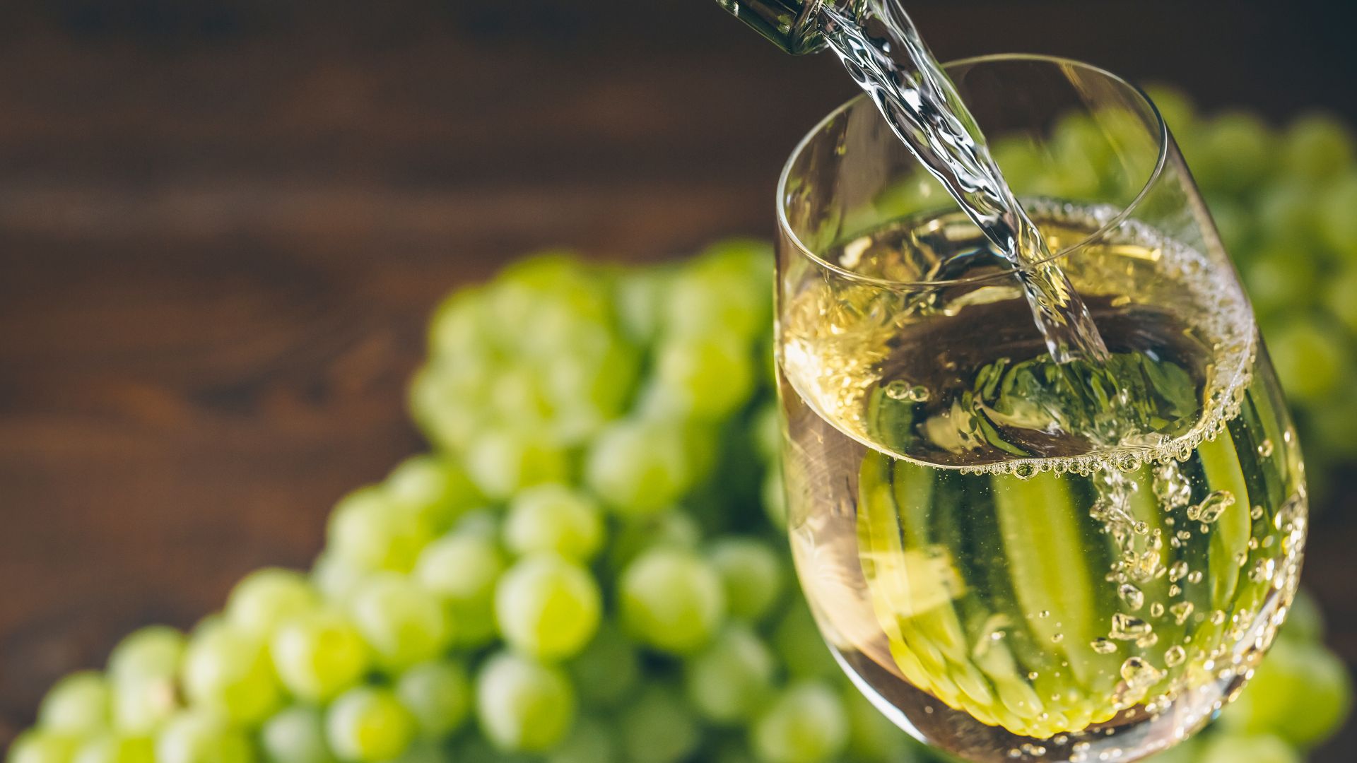 White wine is poured with green grapes in the background