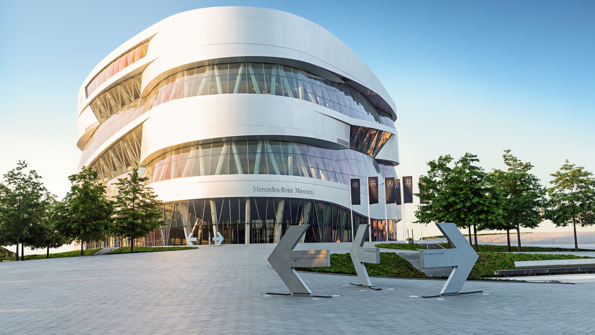 Das Mercedes-Benz Museum in Stuttgart zeigt sich in einem modernen, runden Design. Das Gebäude verfügt über große Glasfenster und ist von Bäumen umgeben.