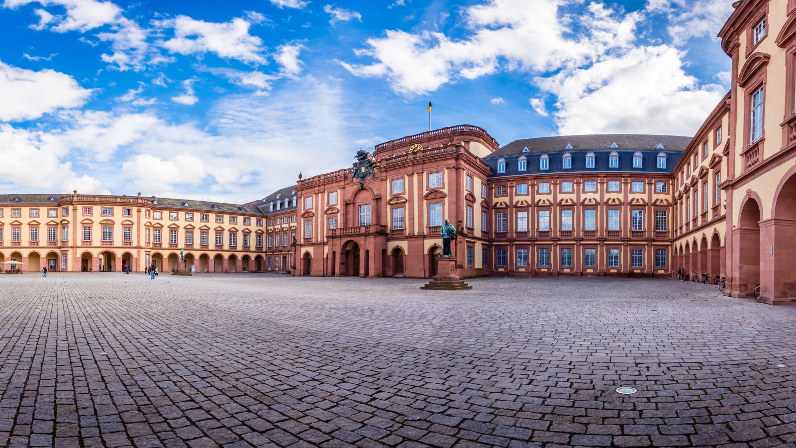 Vaste cour d'honneur du château de Mannheim, avec sa façade baroque, ses pavés et son ciel bleu parsemé de nuages