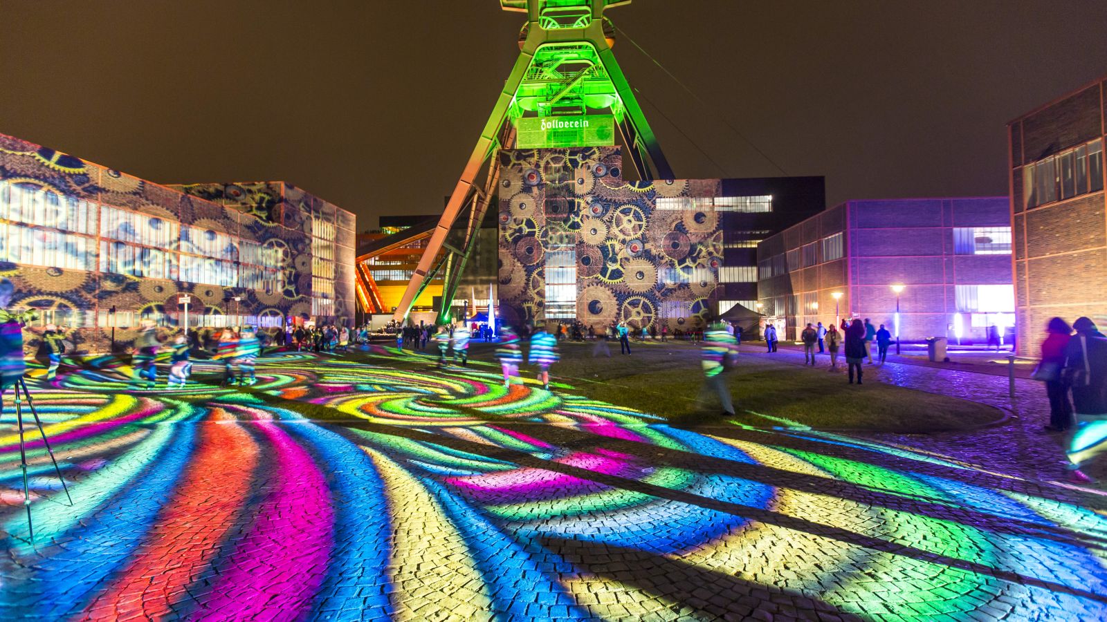 Des lumières colorées projettent des motifs sur le sol et les bâtiments dans un décor nocturne à la mine de Zollverein, lors d'un événement organisé à Essen.