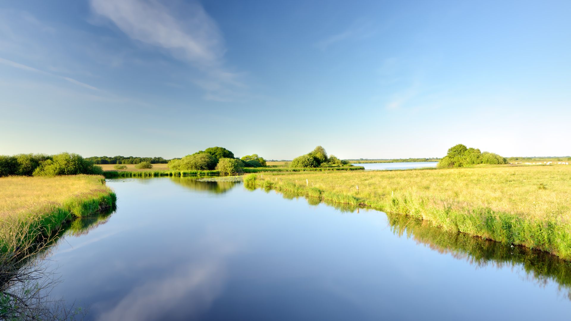 Der ruhige Fluss Hamme fließt durch grüne Felder und Büsche im Gebiet Teufelsmoor, in denen sich der klare blaue Himmel spiegelt