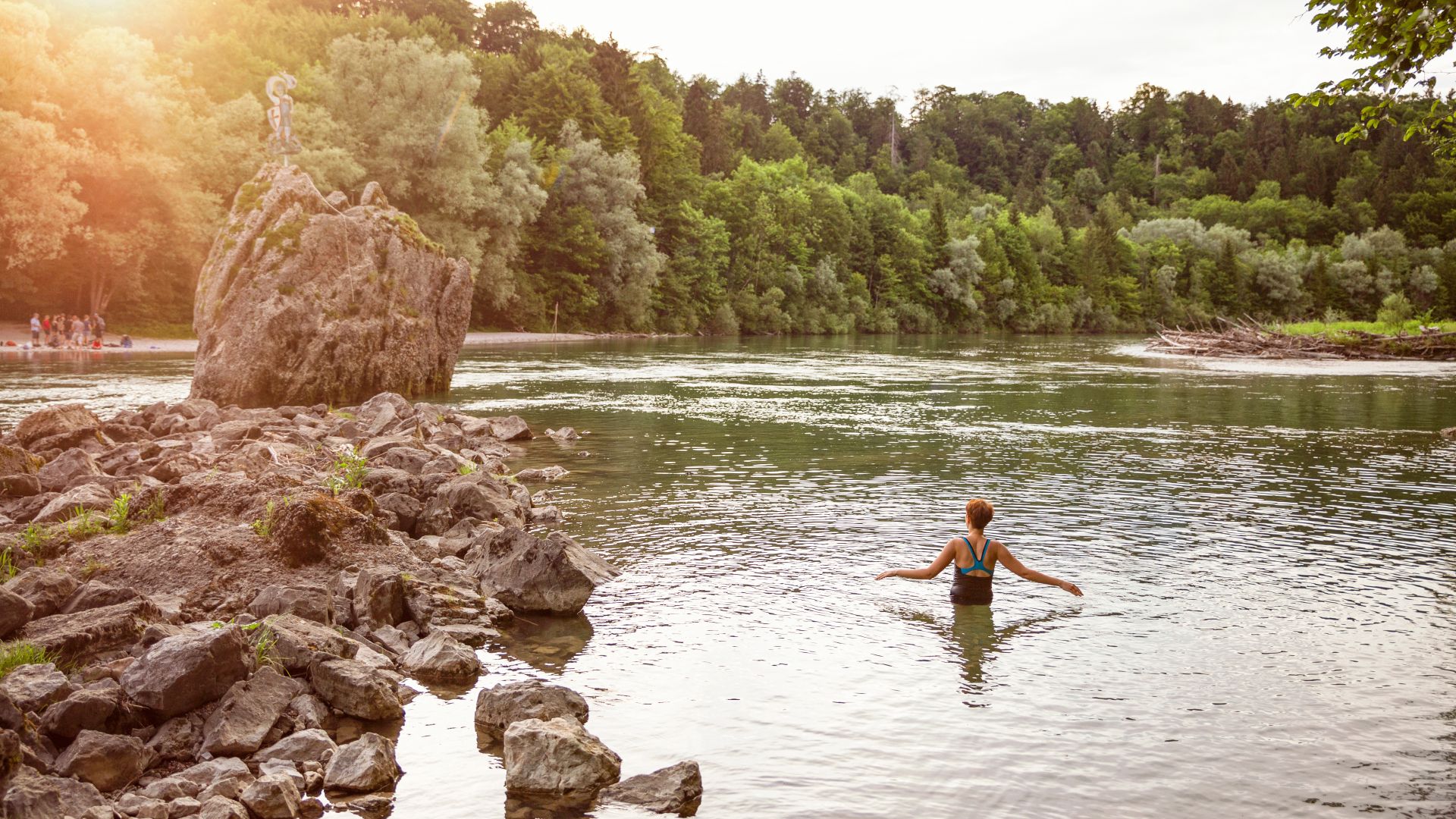 Eine Frau schwimmt in der Isar in München. Die Umgebung ist mit dichten Bäumen bewachsen.