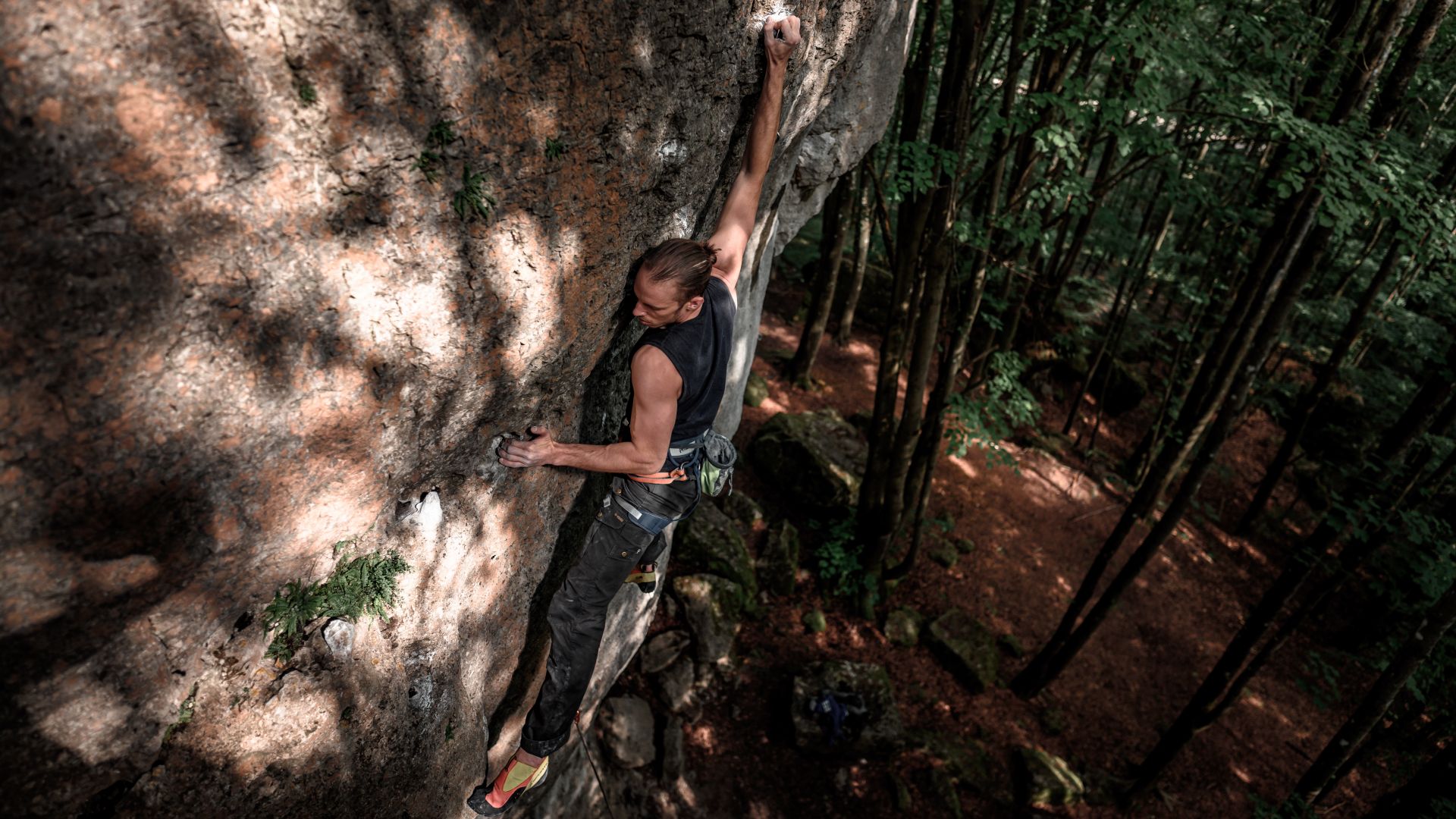Climber on steep rock face in the shaded forest of the Frankenjura