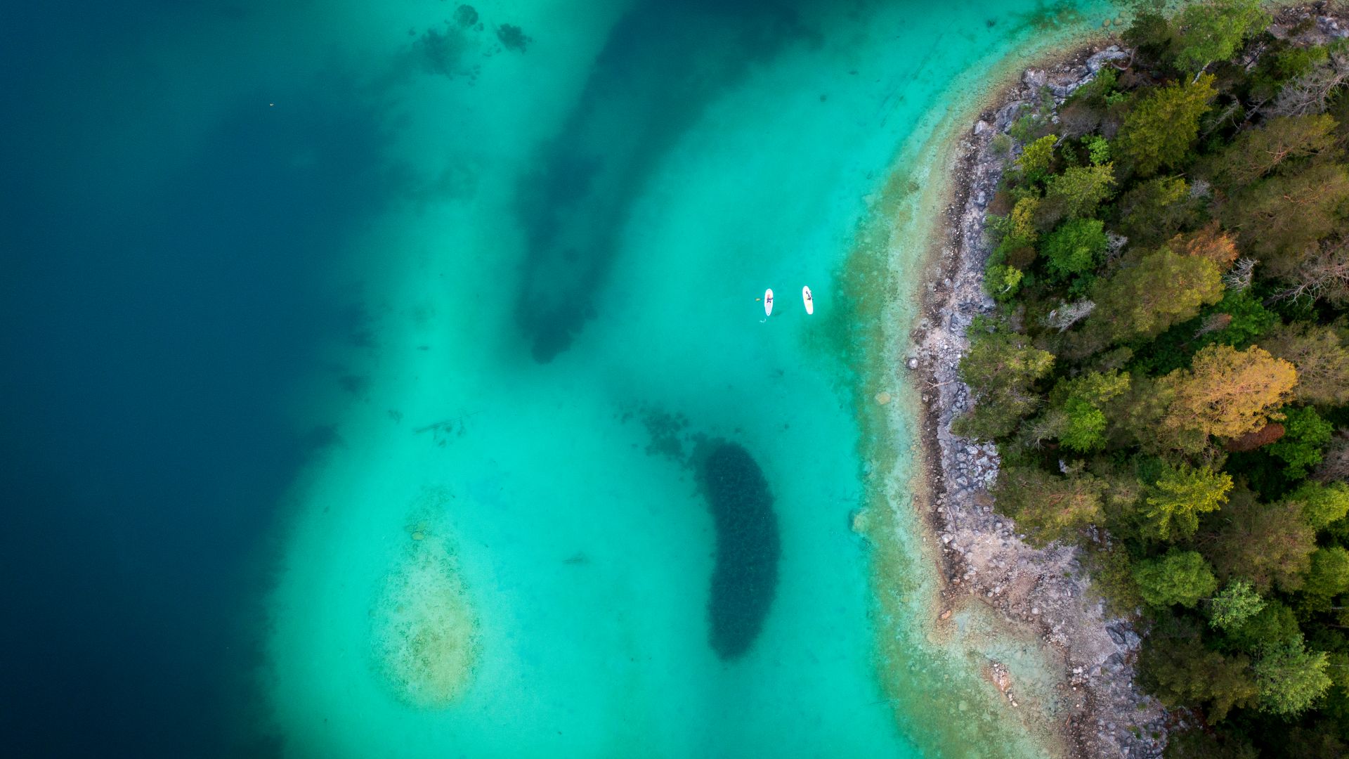 Zwei Personen fahren Stand-up-Paddleboard auf dem klaren türkisfarbenen Wasser des Eibsees bei Sasseninsel in Grainau