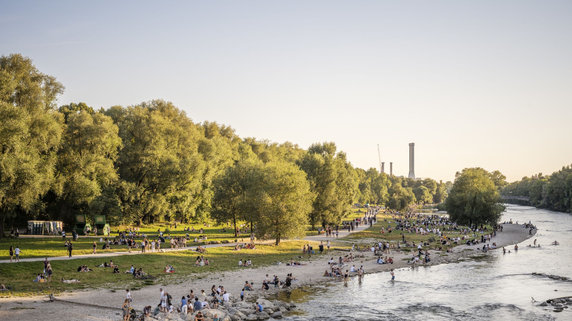 People sit by the Isar on a summer evening at sunset and go for a swim.