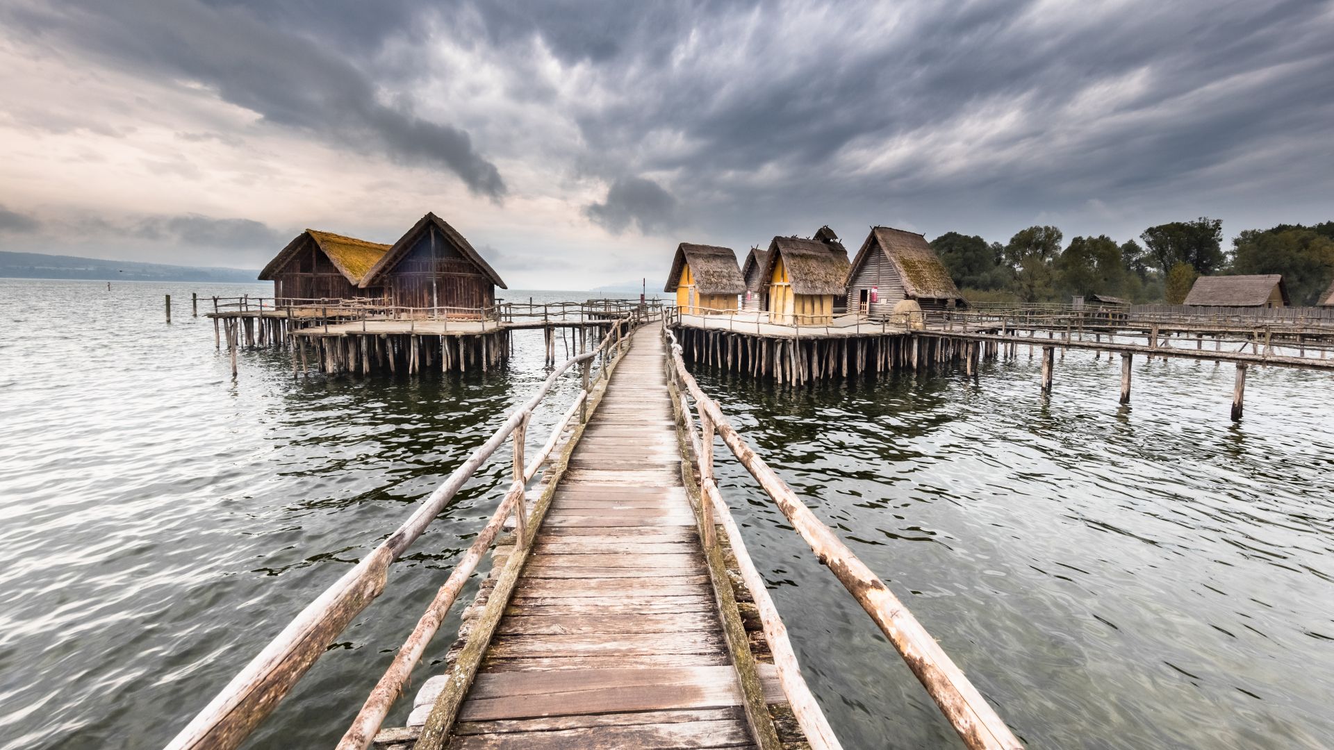 Ein Holzsteg führt zu mehreren prähistorischer Pfahlbauten über dem Wasser des Bodensees in Uhldingen-Mühlhofen.