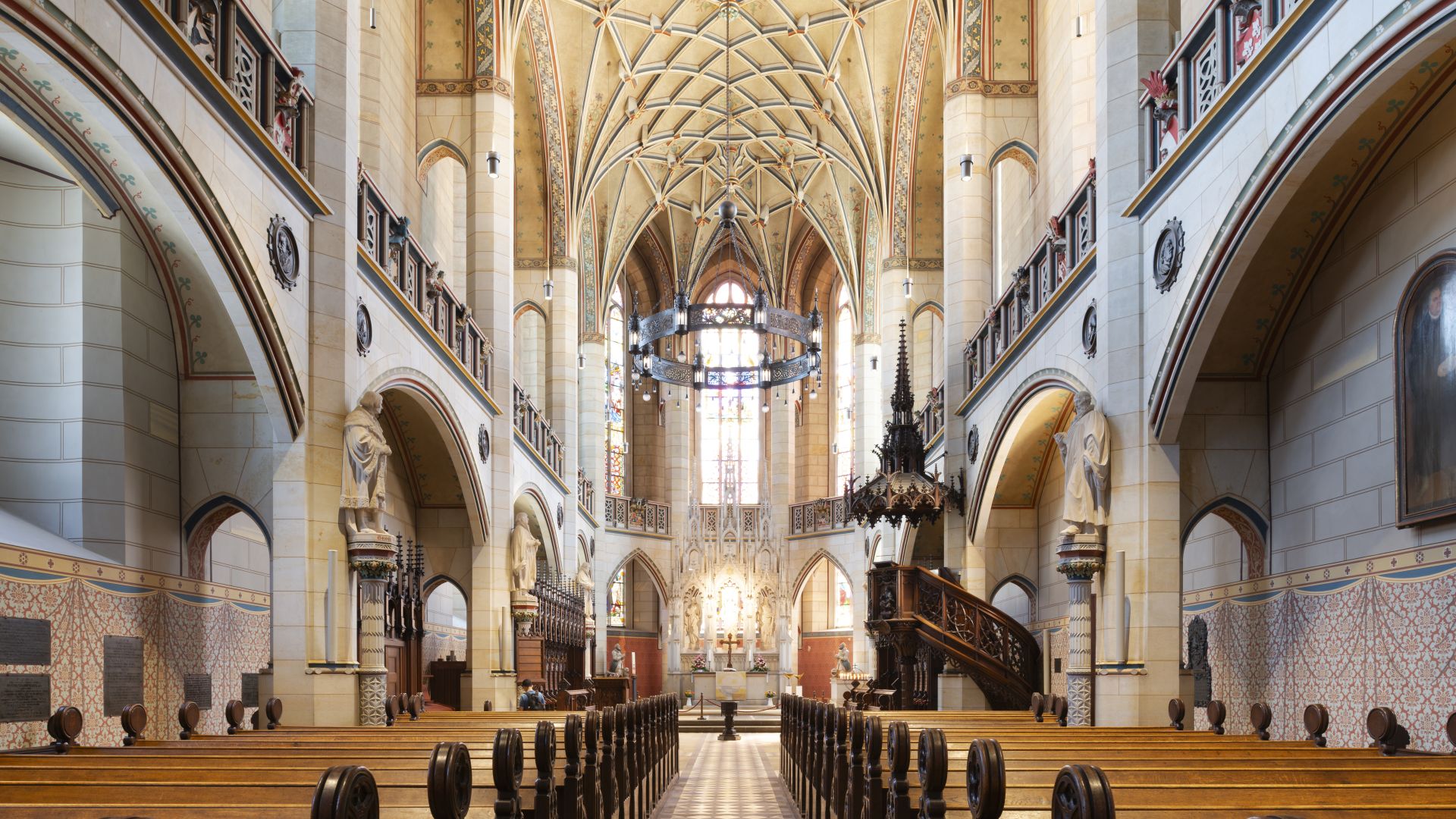 Innenansicht der Schlosskirche in Wittenberg. Die Kirche hat hohe, verzierte Decken, lange Reihen von hölzernen Bänken und bunte Fenster im Hintergrund. Säulen und Bögen schmücken die Wände, und eine imposante Kanzel steht auf der rechten Seite.