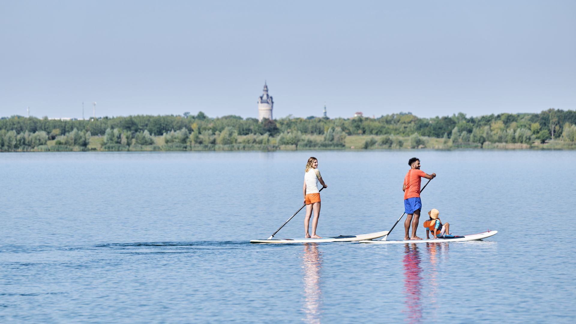 Drei Personen beim Stand-up-Paddling auf einem Leipziger See mit Turm am Horizont