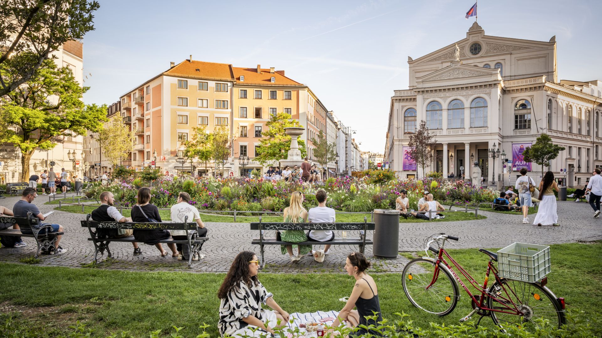 Personas en el Gärtnerplatz con parterres de flores y vista al teatro Gärtnerplatz en Múnich