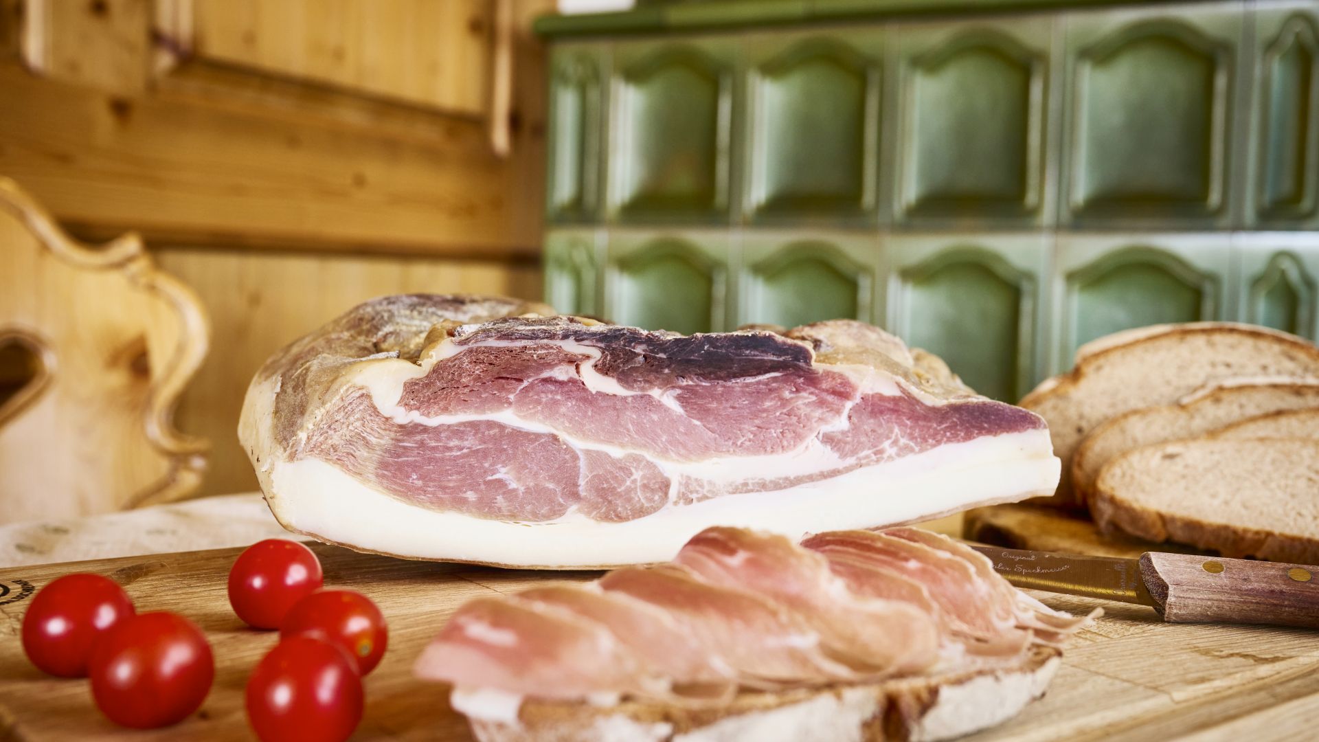Ein Stück Schwarzwälder Schinken auf einem hölzernen Schneidebrett im Gasthaus zum Kreuz in St.Märgen. Daneben liegen kleine Tomaten und Brotscheiben.